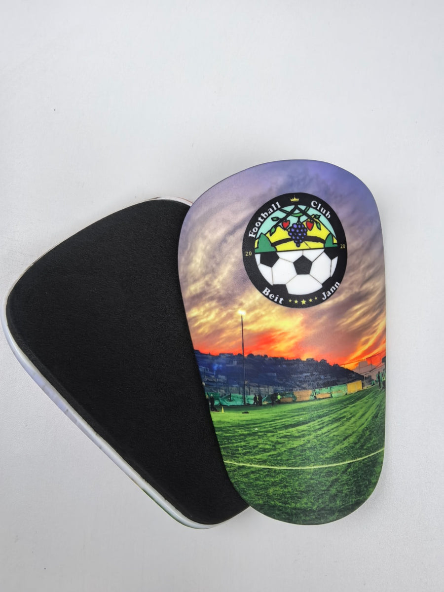 Custom shin guards with a Beit Jann Football Club sunset pitch design